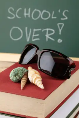Schools out summer vacation seashells on textbook in front of chalkboard