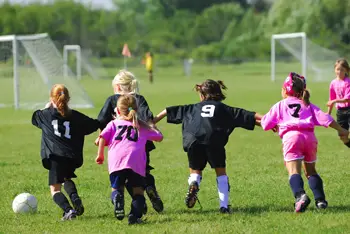 girls playing soccer; young girls on playing field; girls in pink uniforms