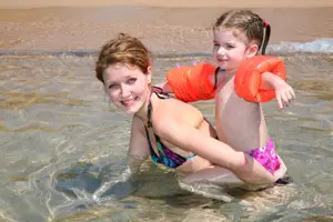 mom and daughter swimming at the beach; mom and daughter in the ocean; mom teaching daughter how to swim