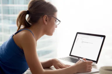 Young,Serious,Woman,In,Glasses,Looks,At,Laptop,Screen,,Writing