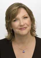 Headshot of a smiling woman with medium-length blonde hair wearing a black top and a blue pendant necklace.
