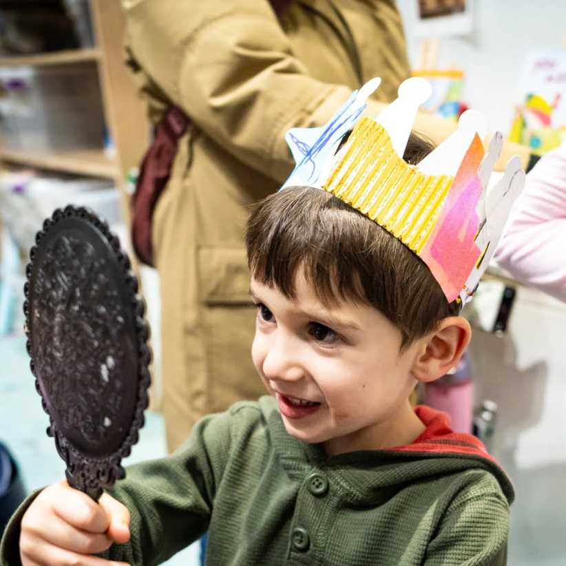 Boy wearing a paper crown looking at himself in a hand held mirror