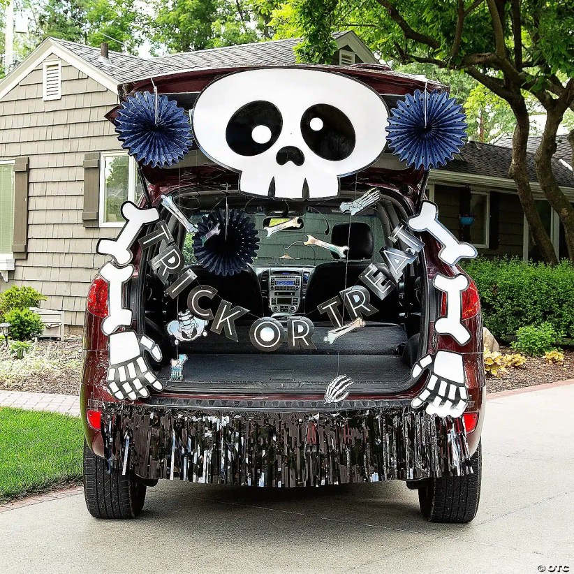 Dark SUV trunk decorated with large cute skull, dangling bones spelling “Trick or Treat,” navy rosettes, and shiny black fringe along bumper.