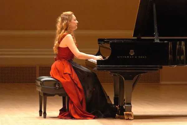 Woman in burgundy gown playing the piano on a stage