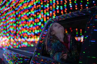 Little girl in a car with her head out the rear window looking up at christmas lights; Drive-Thru Displays
