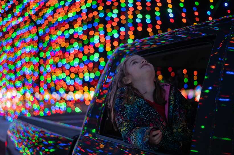 Little girl in a car with her head out the rear window looking up at christmas lights