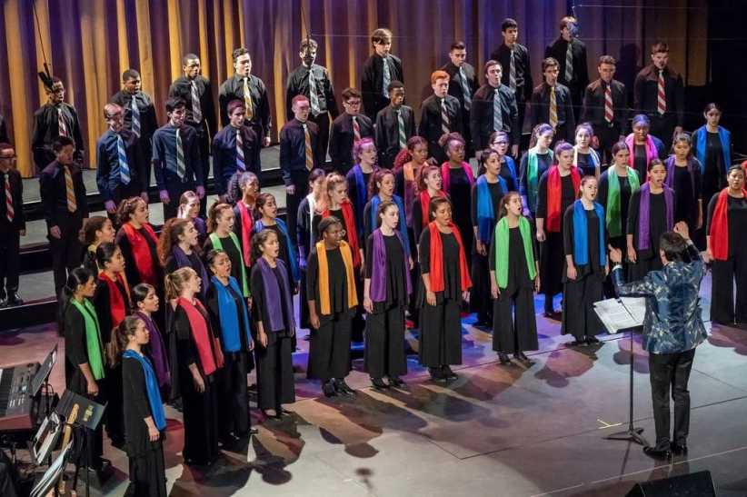 Choir in multi color sashes singing on stage