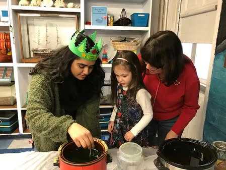 two women helping a young girl dip wax to make candles