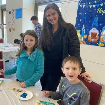 Mother standing next to daughter and seated son participating in a Chanukah activity