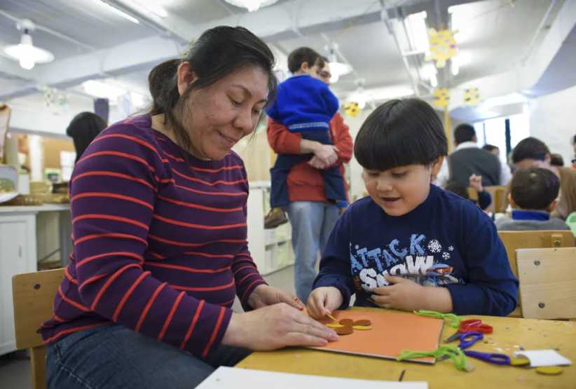 Mother and young son sitting at a table pasting shape on a piece of brown construction paper. 