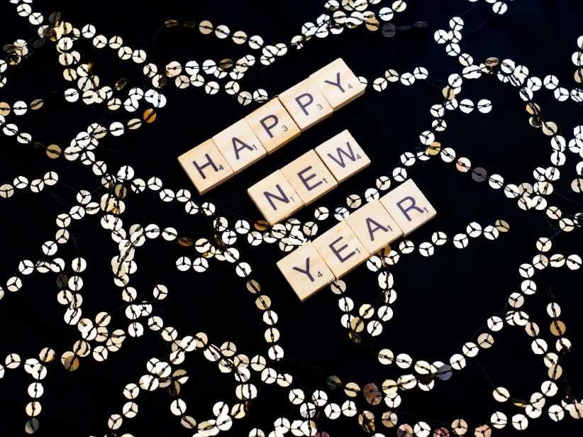 black cloth laid out with silver sequins and on top "happy new year" spelled out in scrabble tiles.
