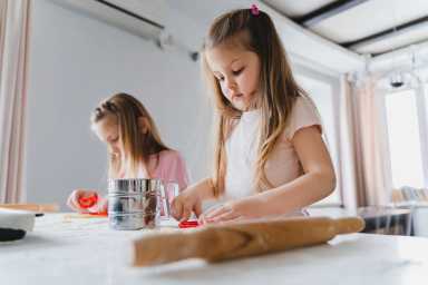 Little girls, sisters cooking homemade heart shaped cookies for valentine's day. Holiday for all lovers. Gift, surprize for mom. Red molds, rolling pin, flour, dough.Handmade family, bakery with kids.