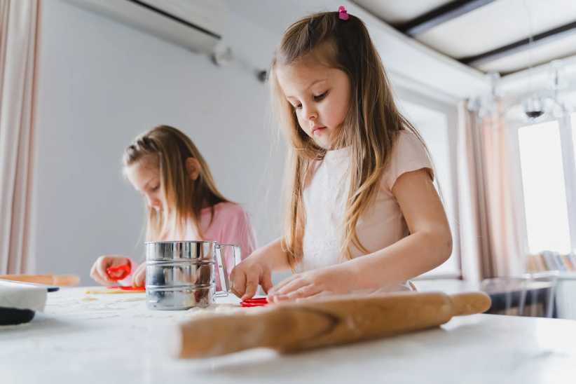 Little girls, sisters cooking homemade heart shaped cookies for valentine's day. Holiday for all lovers. Gift, surprize for mom. Red molds, rolling pin, flour, dough.Handmade family, bakery with kids.