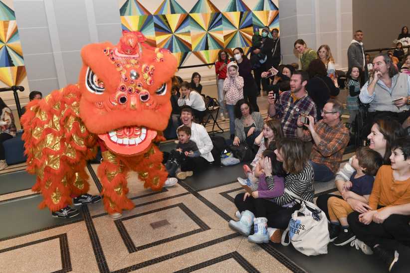 Children sitting on the floor next to a dragon dancer.