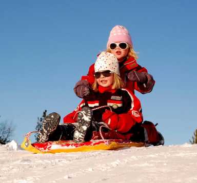 Two girls at the top of a hill sitting on a sled