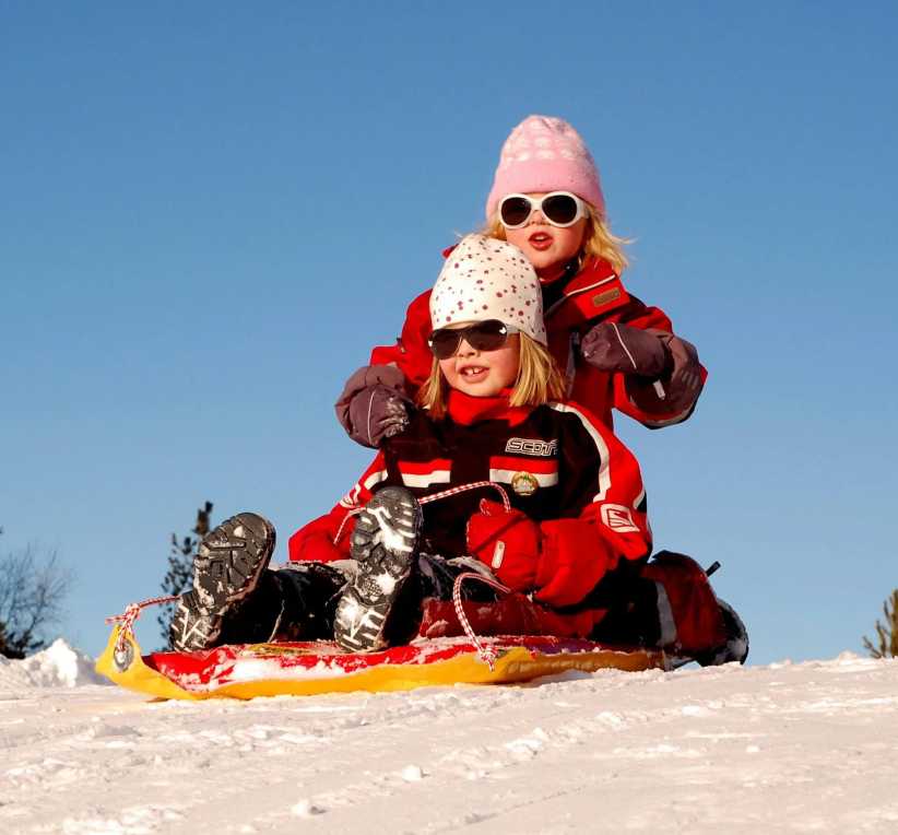 Two girls at the top of a hill sitting on a sled