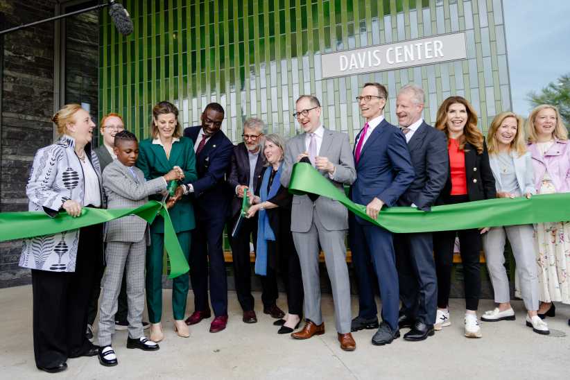 A group of people, dressed formally and casually, celebrate by cutting a large green ribbon in front of a building labeled "Davis Center."