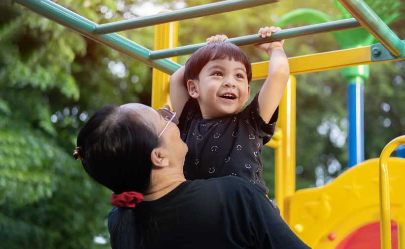Portrait of a little Asian boy hangs by horizontal bar with mother on playground in the sunny day. the concept of a healthy lifestyle. happy childhood.15 Best NYC Playgrounds for Kids & Families in 2026