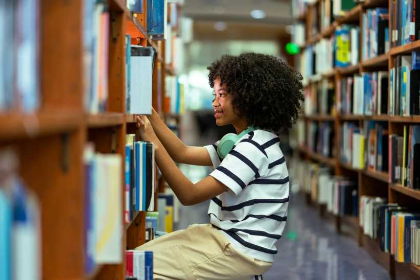 Young girl finding book on bookshelf in the school library. Education knowledge Concept