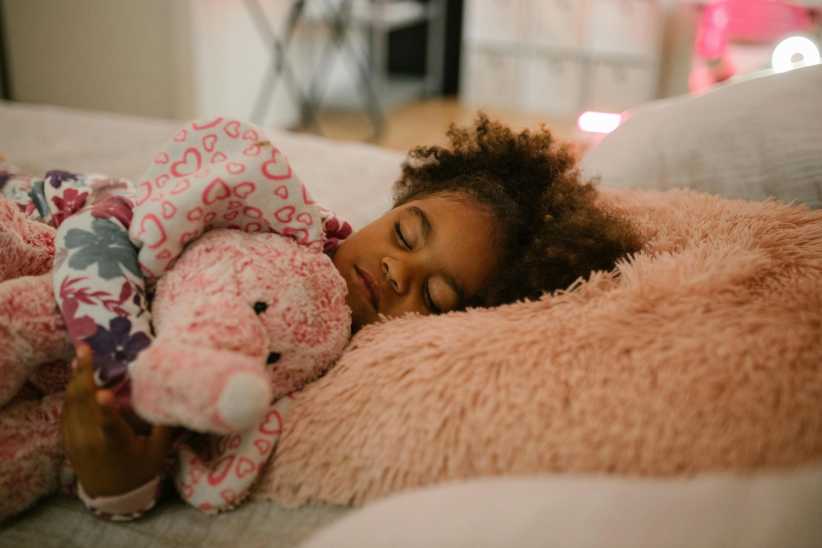Young child sleeping and holding onto stuffed animal, back to school sleep