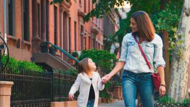 Family Shot With Mother And Daughter Walking Holding Hands Along Urban Street In New York City