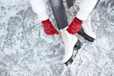 A child's hands lacing up her skates on an ice rink