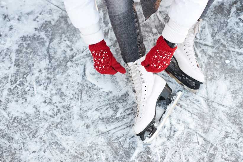 A child's hands lacing up her skates on an ice rink