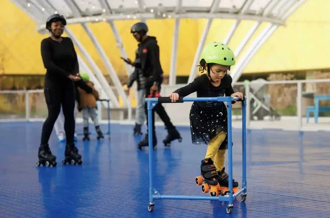 Young child learning to skate as one on the things to do this weekend, wearing a helmet and steadying herself by using a balancer