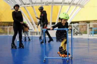 Young child learning to skate as one on the things to do this weekend, wearing a helmet and steadying herself by using a balancer