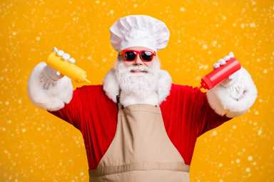 Photo of white grey hair beard santa claus in chef cap squeeze bottle ketchup mustard x-mas christmas eve feast wear apron sunglass isolated  bright yellow color background
