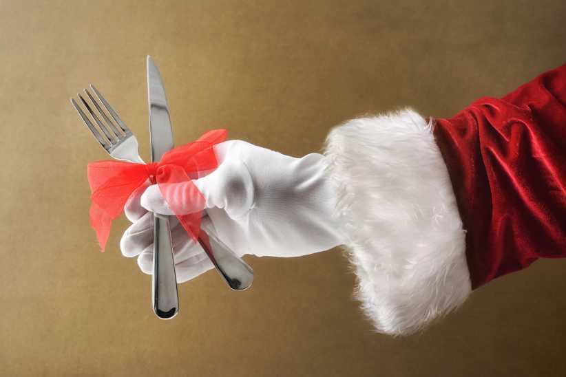 Santa Claus hand holding cutlery with red bow isolated brown