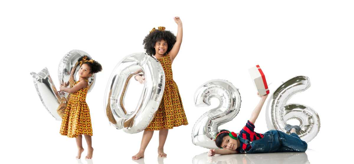 Three children holding silver balloons for the New Year 2026