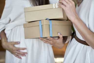 two women , one pregnant, holding neautral boxes with bows