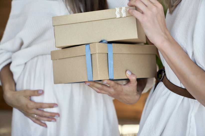 two women , one pregnant, holding neautral boxes with bows