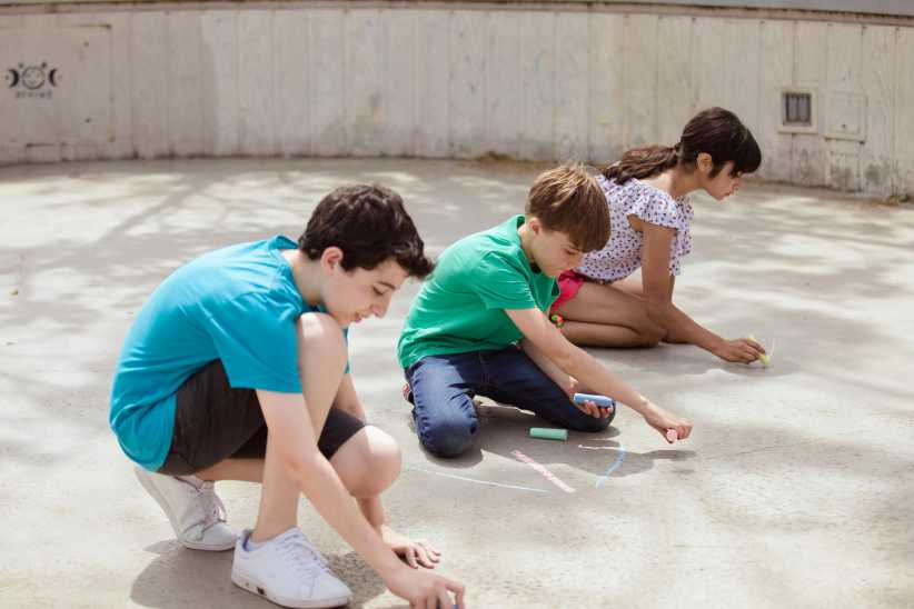 Three kids using sidewalk chalk to draw on the ground.