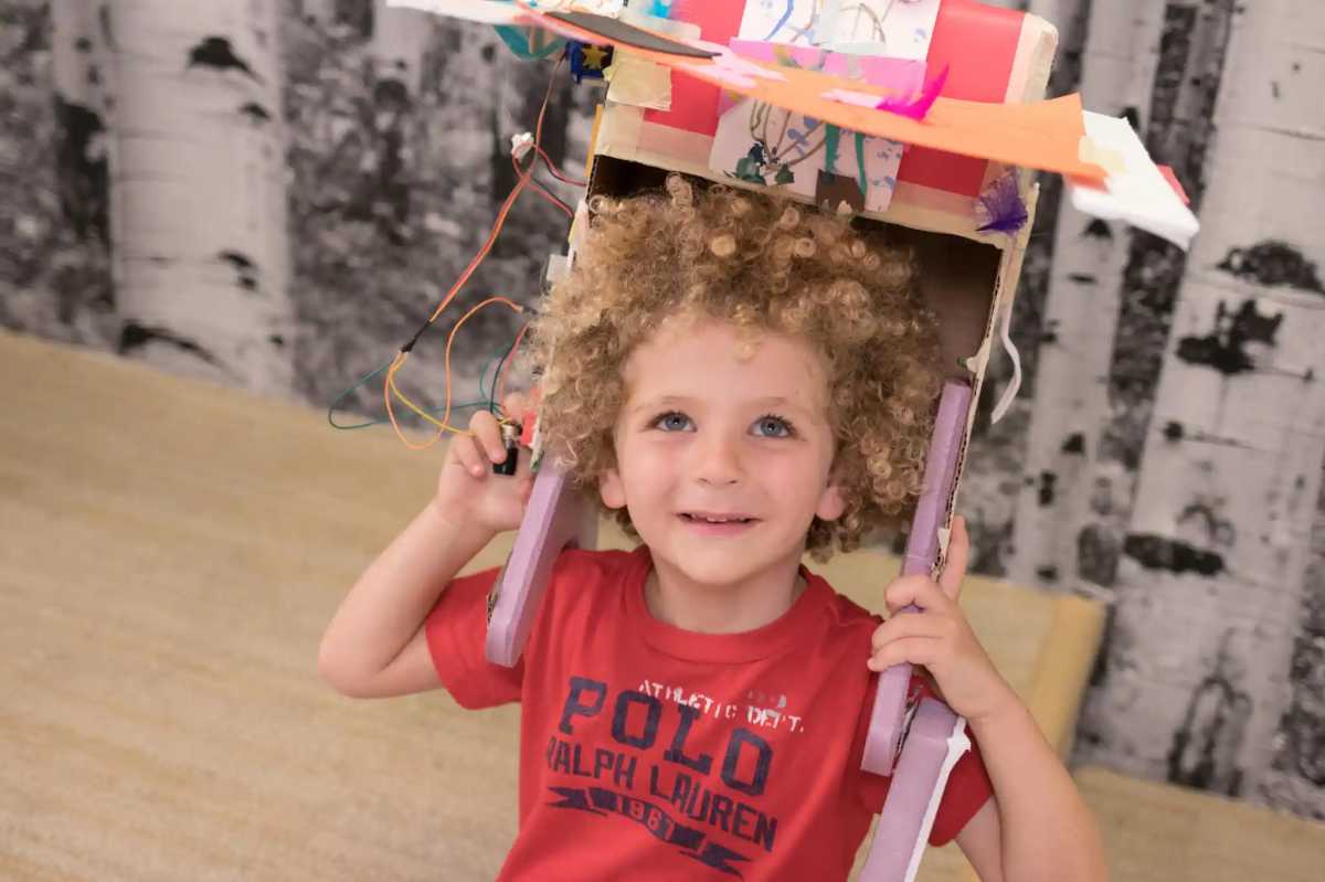 A young child wth thick curly blond hair holding a box over their head at Steamfest, one of the things to do with kids in NYC this weekend