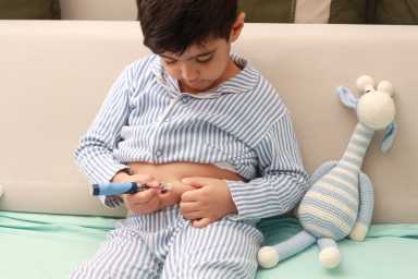 Cute boy with type 1 diabetes taking an insulin shot in the stomach.