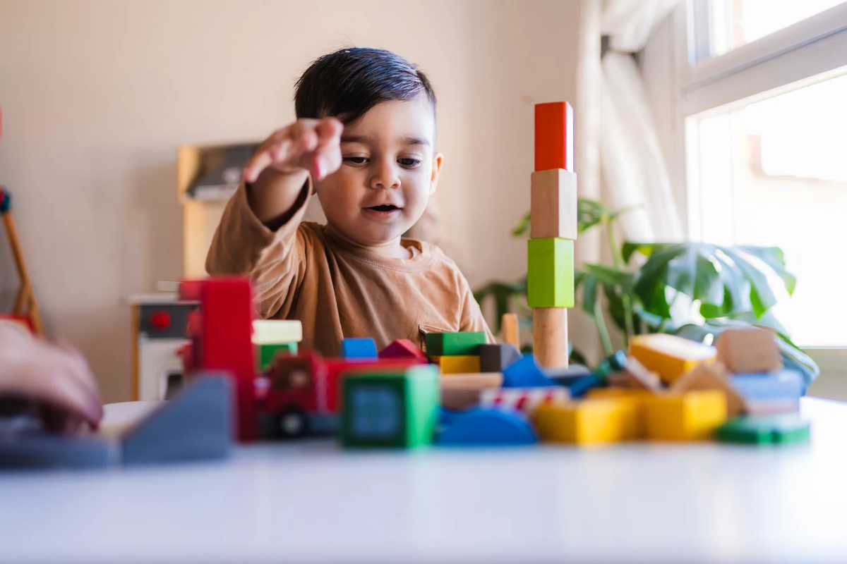 Young child having fun playing with wooden blocks, developing creativity and motor skills as Governor Hochul Announces 2-Care, a Major Step Toward Universal Child Care in New York State
