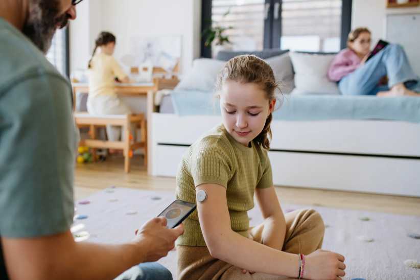 Type 1 diabetes, Diabetic girl with a CGM sensor on her arm. Father using an app to monitor blood sugar levels.