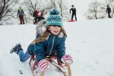 Little girl is lying her belly as she goes down a hill on a sled in the snow.