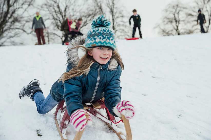Little girl is lying her belly as she goes down a hill on a sled in the snow.