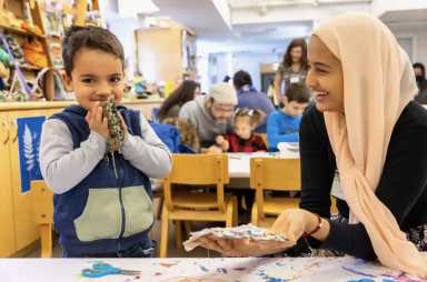 Little boy looking at camera and smiling while mom looks on as they enjoy crafts, one on the things to do this weekend with kids in NYC