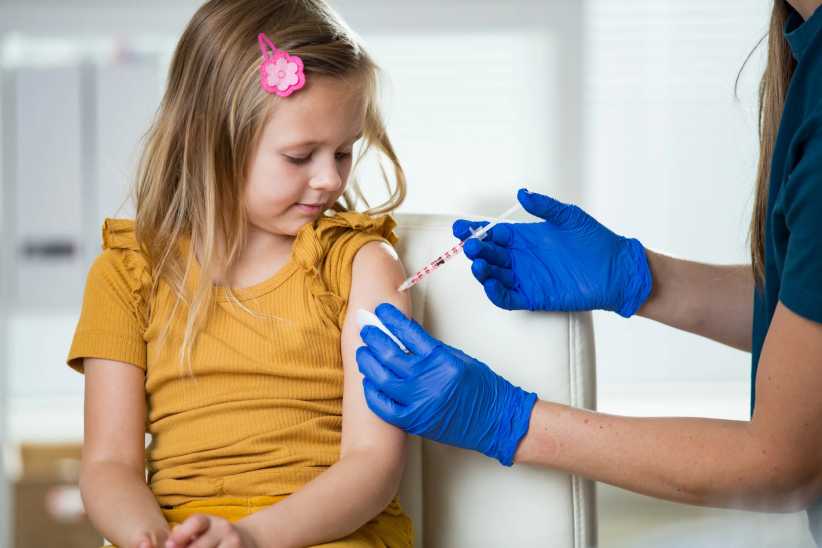 Female nurse with surgical mask and in gloves giving childhood vaccine injection to a young girl in clinic. Children vaccination.