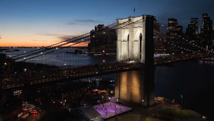 Brooklyn Bridge lit up at night with a view of the ice skating rink