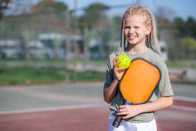 Portrait little teenage girl playing pickleball game, pickleball yellow ball with paddle in hands, outdoor sport leisure kids activity
