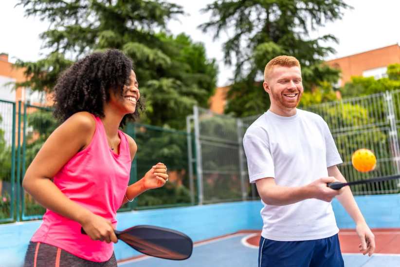 Team playing pickelball in an outdoor court while having fun together and smiling