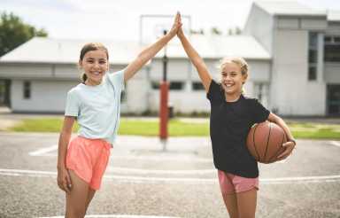 Two tweens holding up their hands, one carrying a basketball.