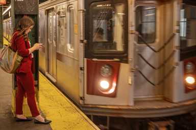 Young woman in a red dress checking her mobile phone standing on the platform in front of the approaching subway train. The MTA App Just Made Getting Around With Kids a Bit Easier