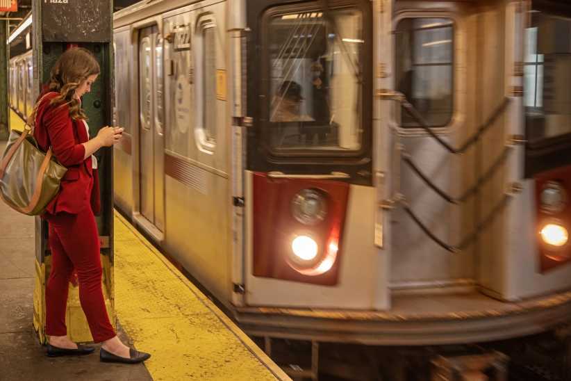 Young woman in a red dress checking her mobile phone standing on the platform in front of the approaching subway train. The MTA App Just Made Getting Around With Kids a Bit Easier