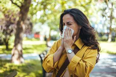 Portrait of woman in yellow top with napkin blowing nose, Why Spring Allergies Feel Worse in NYC: An Allergist Explains What Families Should Expect